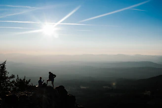Hikers pausing on a rocky outcrop with vast valleys beneath.