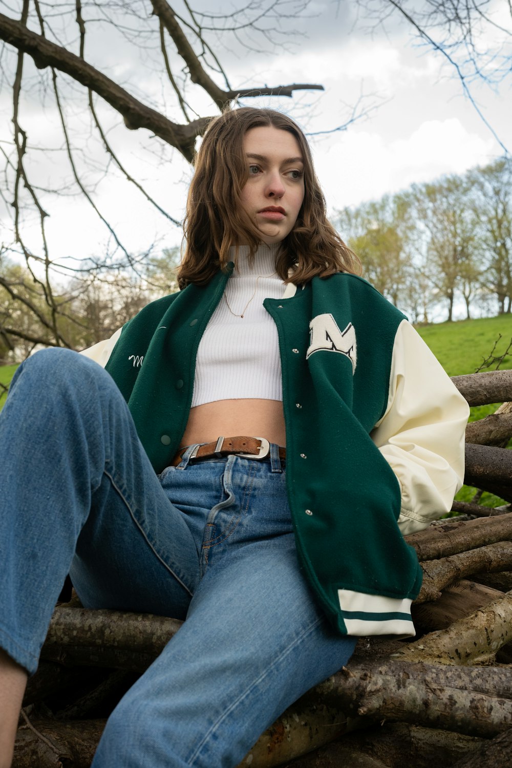 a woman with varsity jacket sitting on top of a tree branch