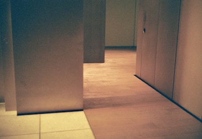 A minimalist interior space with geometric architectural elements. Light wood flooring is contrasted with soft beige walls, partially divided by vertical panels. The overall design is simplistic yet sophisticated, with a calm ambiance.