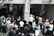 A crowd of people, primarily men and boys wearing traditional attire including fur hats and prayer shawls, are entering through a gateway. There is a separate entrance for women on the right. Several Israeli flags can be seen above the entrance.