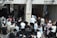 A crowd of people, primarily men and boys wearing traditional attire including fur hats and prayer shawls, are entering through a gateway. There is a separate entrance for women on the right. Several Israeli flags can be seen above the entrance.