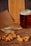 A glass of dark beer sits on a wooden surface next to dried fish and a pile of nuts, all arranged on top of printed paper. A wooden cutting board is visible in the background.