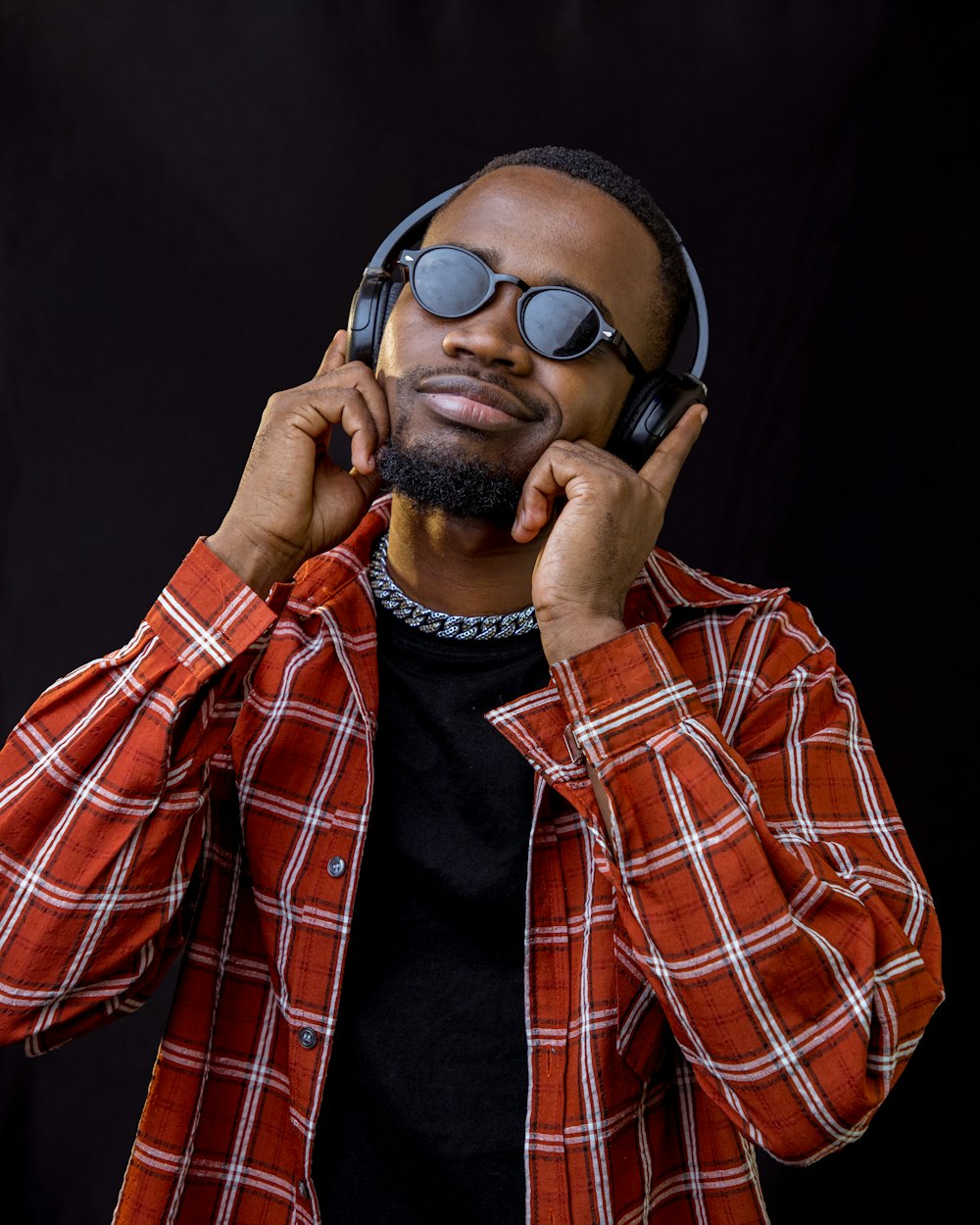 a man wearing sunglasses and a plaid shirt is listening to headphones