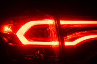 Close-up view of an illuminated red car taillight with clear lens details and glowing LED lights. The bright red light creates a strong contrast against the dark background.