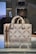 A stylish designer handbag made from a textured material featuring a repeating geometric pattern with the brand name prominently displayed. The colors consist of subtle shades of brown and beige, creating a sophisticated look. The bag is placed on a reflective surface in a well-lit setting.