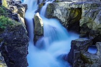 Majestic waterfall cascading between rugged rock formations with vibrant greenery on the sides, creating a dramatic and serene natural scene.