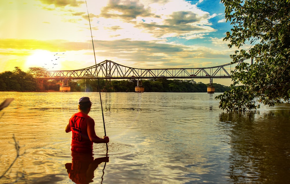 a man fishing on a river with a bridge in the background