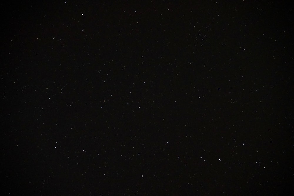 a night sky with stars and a plane in the distance