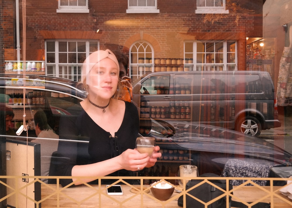a woman holding a cup in front of a store window