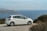 A pristine rental car parked on a scenic road with ocean views in Okinawa.