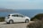 A pristine rental car parked on a scenic road with ocean views in Okinawa.