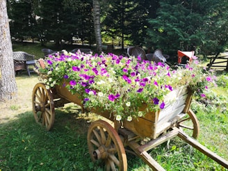 A rustic vintage wooden garden cart filled with fresh flowers and gardening tools, set against a lush garden backdrop.
