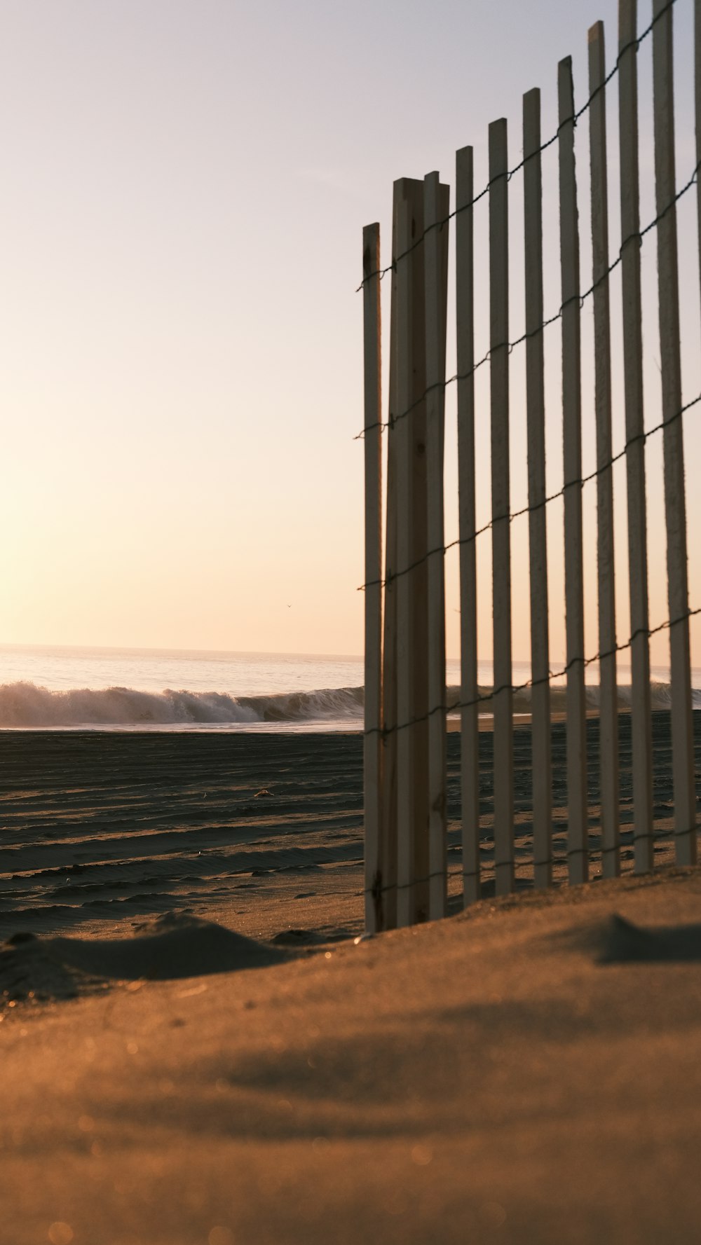 a fence on a beach with a body of water in the background