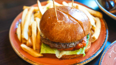 A juicy hamburger with crispy golden fries on a rustic wooden table.