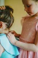 a little girl helping another girl put on a dress