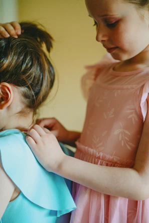a little girl helping another girl put on a dress
