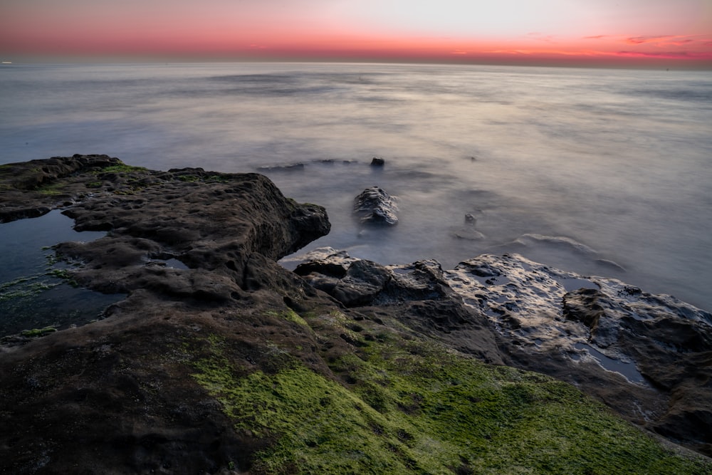 the sun is setting over the water and rocks