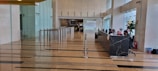 A spacious lobby area with polished floors and a row of modern turnstiles leading to a corridor. On the right, a long black marble reception desk with several people sitting and working. Glass walls and indoor plants enhance the open and bright atmosphere.