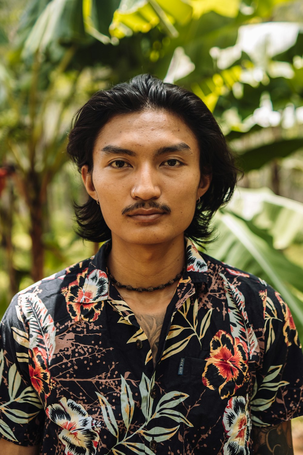 a man with a moustache standing in front of some plants