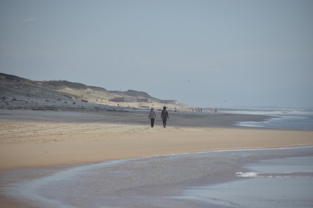 two people walking on a beach next to the ocean