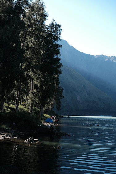 A serene lakeside campsite at dawn with a Red Water Lake tent pitched beside a calm water reflection.