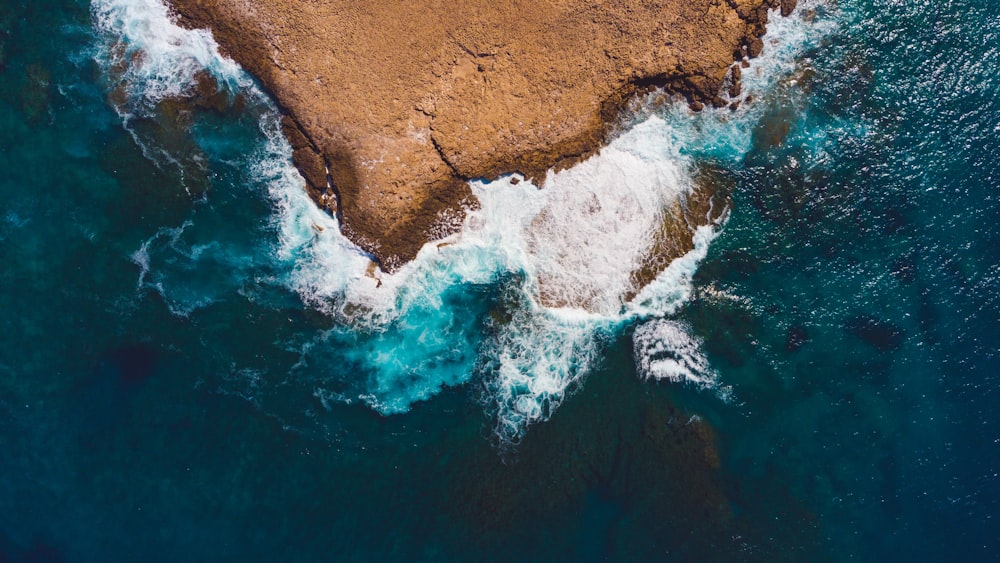 an aerial view of the ocean with waves crashing on the rocks