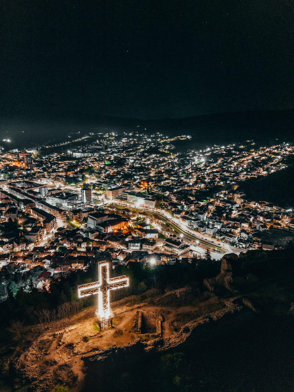 Una ciudad de noche con una cruz iluminada en primer plano