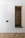 A minimalist built-in cabinet with a white exterior and a recessed wooden alcove. The alcove has a small green cushion and six black pegs arranged on the back wall. The floor features a herringbone wood pattern.