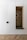 A minimalist built-in cabinet with a white exterior and a recessed wooden alcove. The alcove has a small green cushion and six black pegs arranged on the back wall. The floor features a herringbone wood pattern.