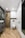 A modern bathroom featuring wooden herringbone-patterned flooring and walls. A sleek glass shower enclosure with black fixtures sits next to a wall-mounted toilet. Minimalistic white cabinets offer storage. The room is well-lit with recessed ceiling lights.