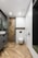 A modern bathroom featuring wooden herringbone-patterned flooring and walls. A sleek glass shower enclosure with black fixtures sits next to a wall-mounted toilet. Minimalistic white cabinets offer storage. The room is well-lit with recessed ceiling lights.