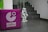 A small humanoid robot stands at the base of a staircase with tiled steps. To the left, a purple cube with the logo and words 'Goethe Institut' is visible. The floor is also tiled, and the surrounding walls are mostly plain.