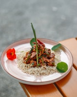 A chef carefully plating a dish of lamb and rice with vibrant spices and sauce drizzles.