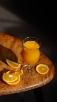 Uma taça com suco de laranja, laranjas cortadas em fatias ao lado, sobre uma mesa amadeirada