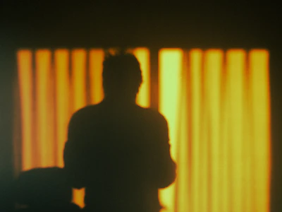 A shadowed silhouette of a masked figure against a glowing gold backdrop.