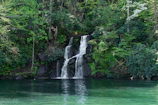 A hidden waterfall cascading into a crystal-clear pool surrounded by lush green forest.