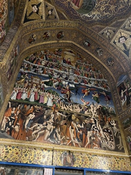 An intricate religious fresco depicting many figures engaged in various scenes, possibly representing heaven and hell. The top contains a divine scene with angels and a central figure surrounded by swirling clouds. Below, a contrasting depiction involves figures amidst flames, demons, and chaotic movement. The art is detailed, with figures dressed in historical garments.