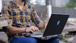 A person using a laptop outdoors with a blurred city background.
