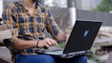Person typing on a laptop outdoors with a blurred city background.