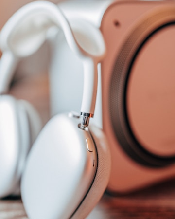 Close-up view of a pair of white over-ear headphones with a blurred background, possibly another audio device.