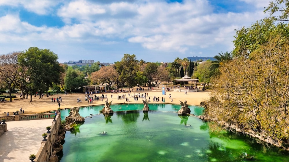 people are walking around a green pond in a park