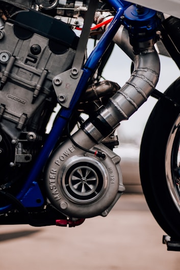 A close-up view of a motorcycle engine featuring a prominently displayed turbocharger with the words 'MASTER POWER' and model number 'NB132'. The engine is assembled with metallic components, including bolts and detailed pipework. The structure includes blue metallic elements in the frame connecting the parts.