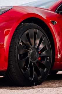A set of sporty black alloy wheels mounted on a red hatchback in a showroom.