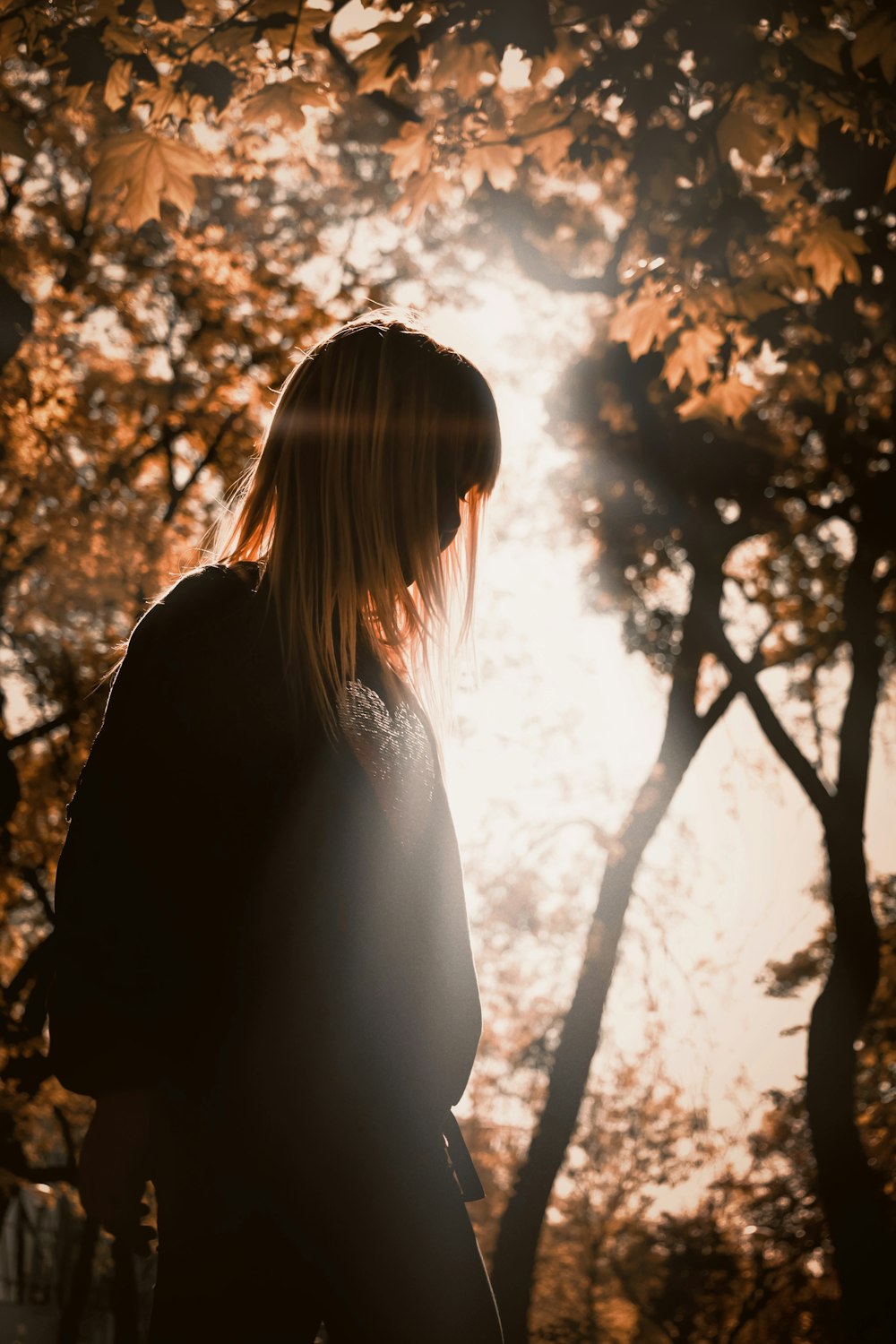 a woman standing in front of a tree with the sun shining through it
