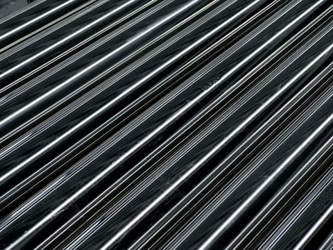 Multiple parallel, glossy, dark metallic pipes are arranged diagonally across the frame, reflecting light and creating a smooth, industrial texture.