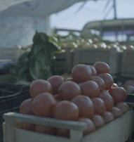 Close-up of ripe, deep crimson tomatoes arranged on a rustic wooden crate at a local farmers market.
