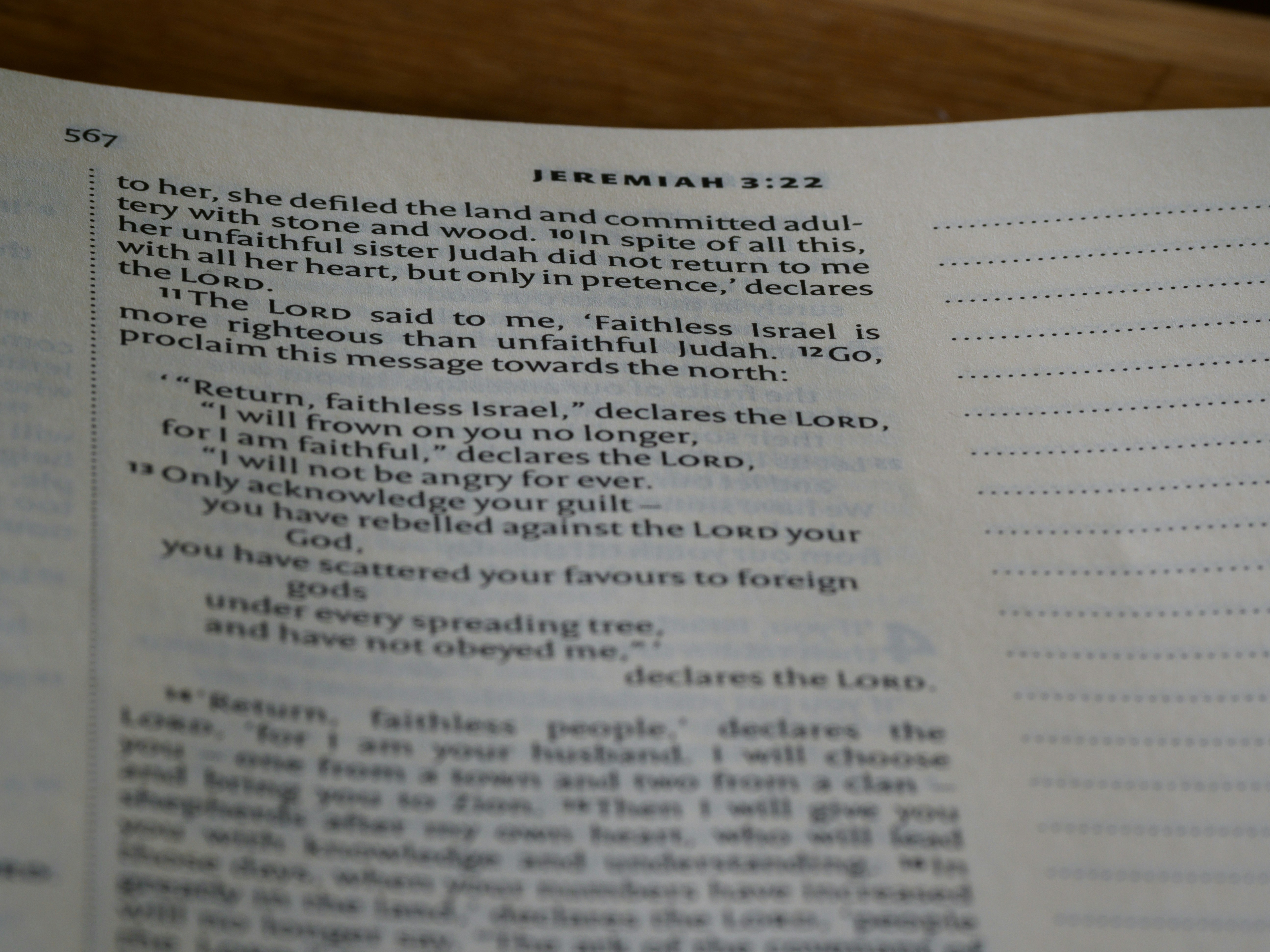 A close-up view of an open book showing text from the Bible, specifically Jeremiah 3:22, with printed lines and numbers visible on a slightly curved page.