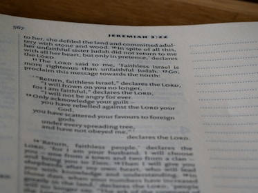 A close-up view of an open book showing text from the Bible, specifically Jeremiah 3:22, with printed lines and numbers visible on a slightly curved page.