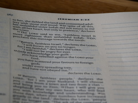 A close-up view of an open book showing text from the Bible, specifically Jeremiah 3:22, with printed lines and numbers visible on a slightly curved page.