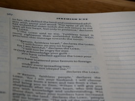 A close-up view of an open book showing text from the Bible, specifically Jeremiah 3:22, with printed lines and numbers visible on a slightly curved page.